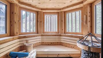 Una sauna de madera con bancos, ventanas amplias y una chimenea de piedra.