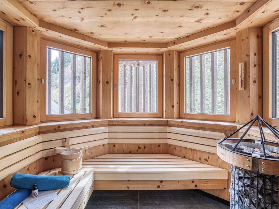 Una sauna de madera con bancos, ventanas amplias y una chimenea de piedra.