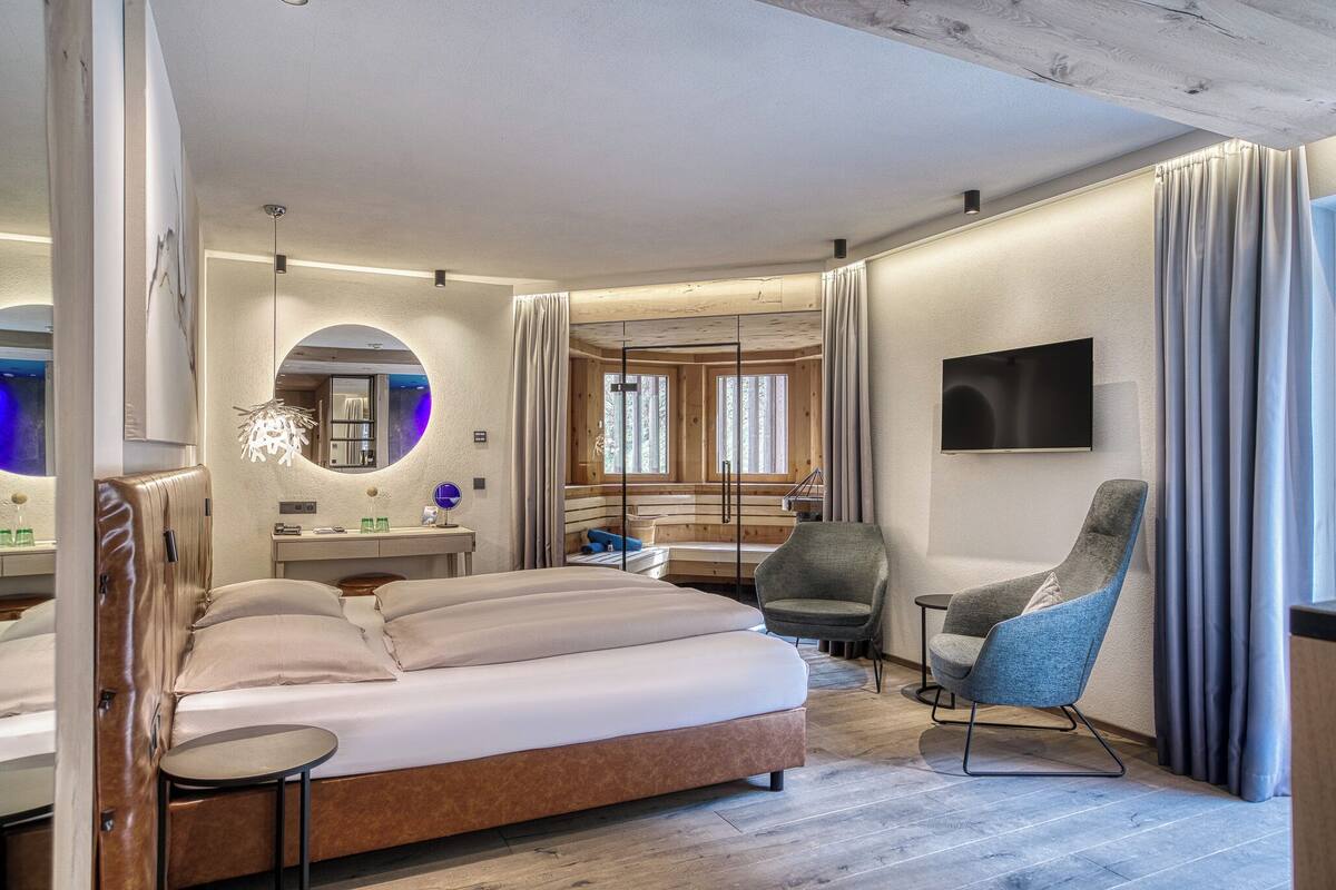 Ein modernes Hotelzimmer mit einem großen Bett, einem Schreibtisch, einem Sessel und einem Fernseher.