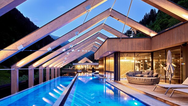 Ein moderner Poolbereich mit Holzterrasse, einer Liege und einem gläsernen Raum mit Blick auf den Pool.