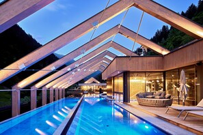 Een modern zwembadgedeelte met een houten terras, een lounge stoel, en een glazen ruimte met uitzicht op het zwembad.