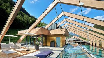 Un área de piscina exterior moderna con vigas de madera, sillones de descanso y una piscina cubierta de cristal.