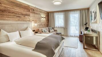 A hotel room with a wooden accent wall, a bed with white bedding, a desk with a mirror, and a large window with sheer curtains.