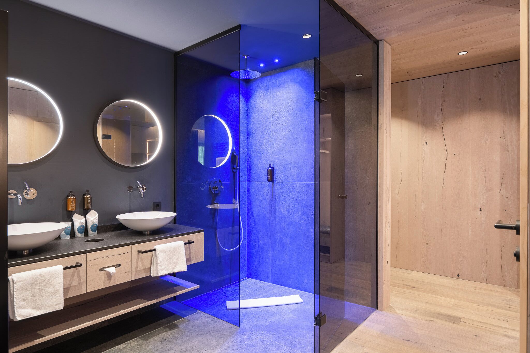A modern bathroom with two sinks, a glass-enclosed shower, and a wooden door.