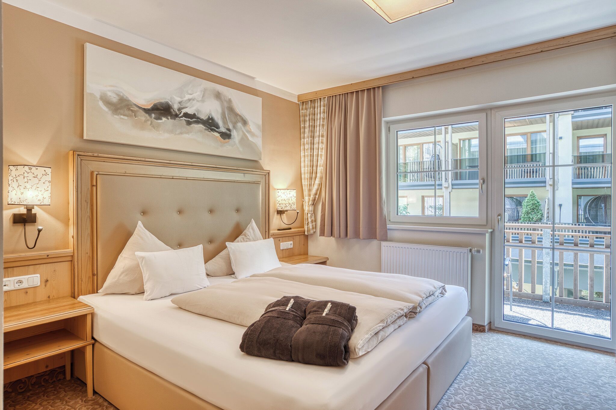 A hotel room with a large bed, a headboard, a nightstand, a lamp, a window with curtains, and a view of the outside.