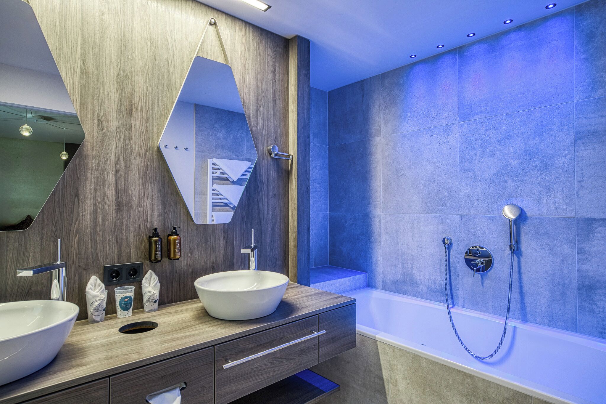 A modern bathroom with a large mirror, two sinks, a bathtub, and a shower.