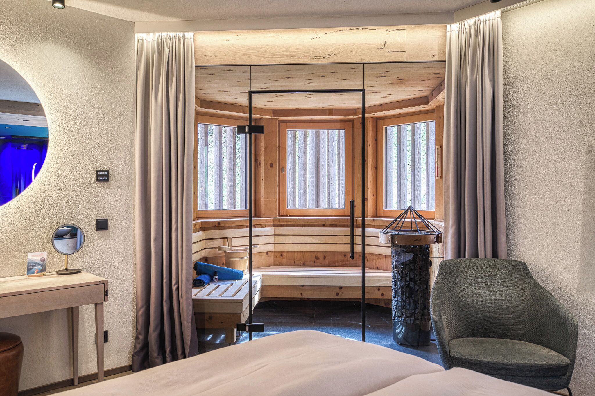 A room with a bed, a desk with a mirror, a chair, a stone table, and a window with curtains.