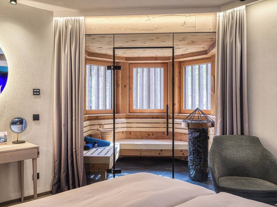 A room with a bed, a desk with a mirror, a chair, a stone table, and a window with curtains.