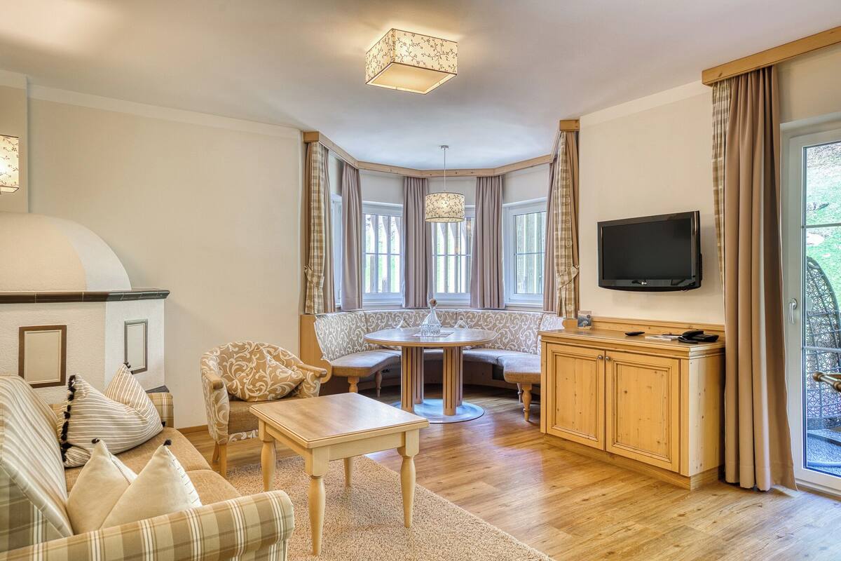 Ein gemütliches Wohnzimmer mit Sofa, rundem Tisch, Fernseher und einem Fenster mit Vorhängen.