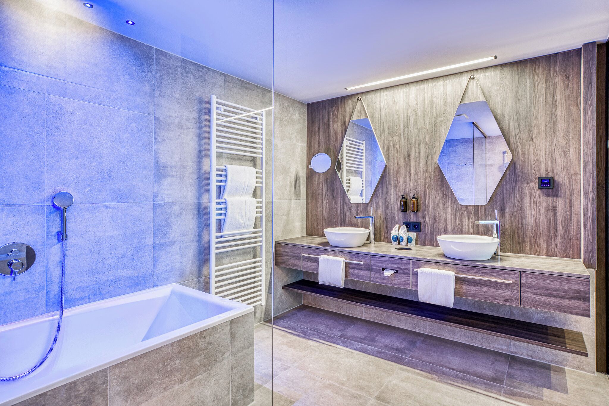 Un baño moderno con una bañera, dos lavamanos, un espejo grande y un perchero para toallas.