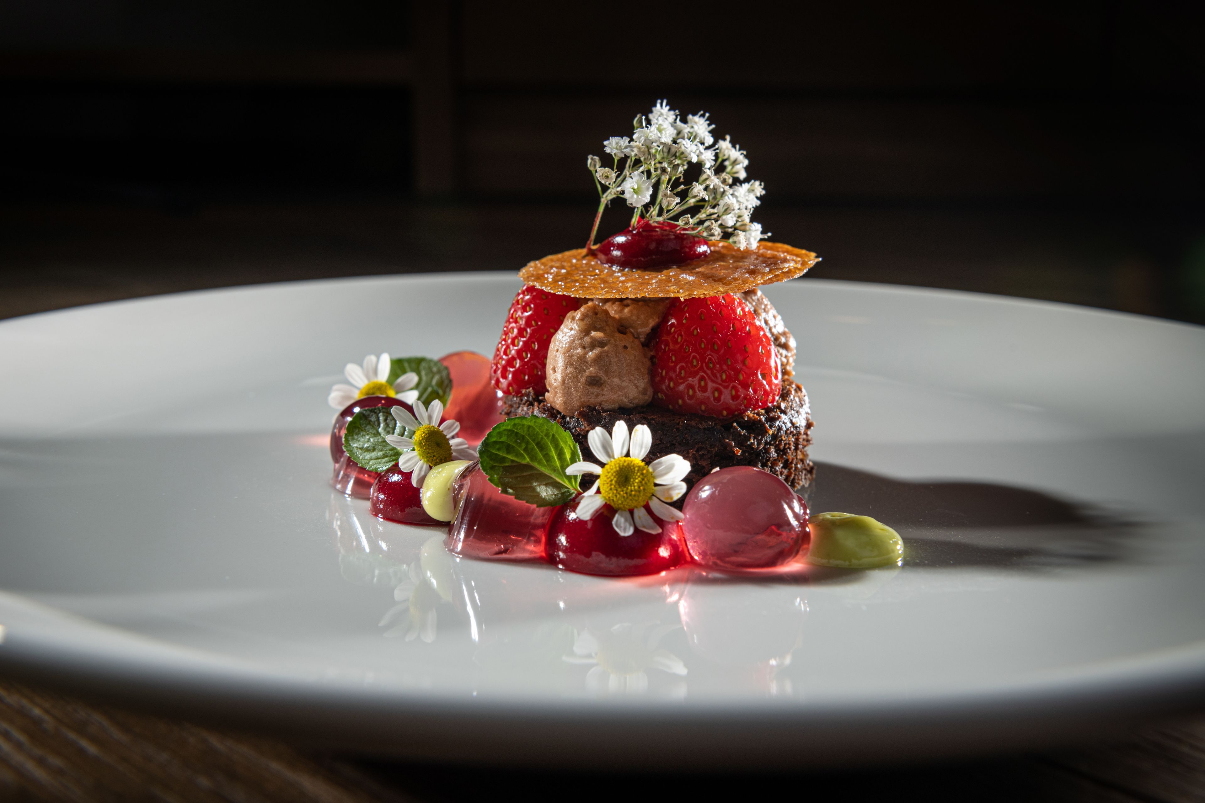 A dessert on a white plate with strawberries, ice cream, and decorative flowers.