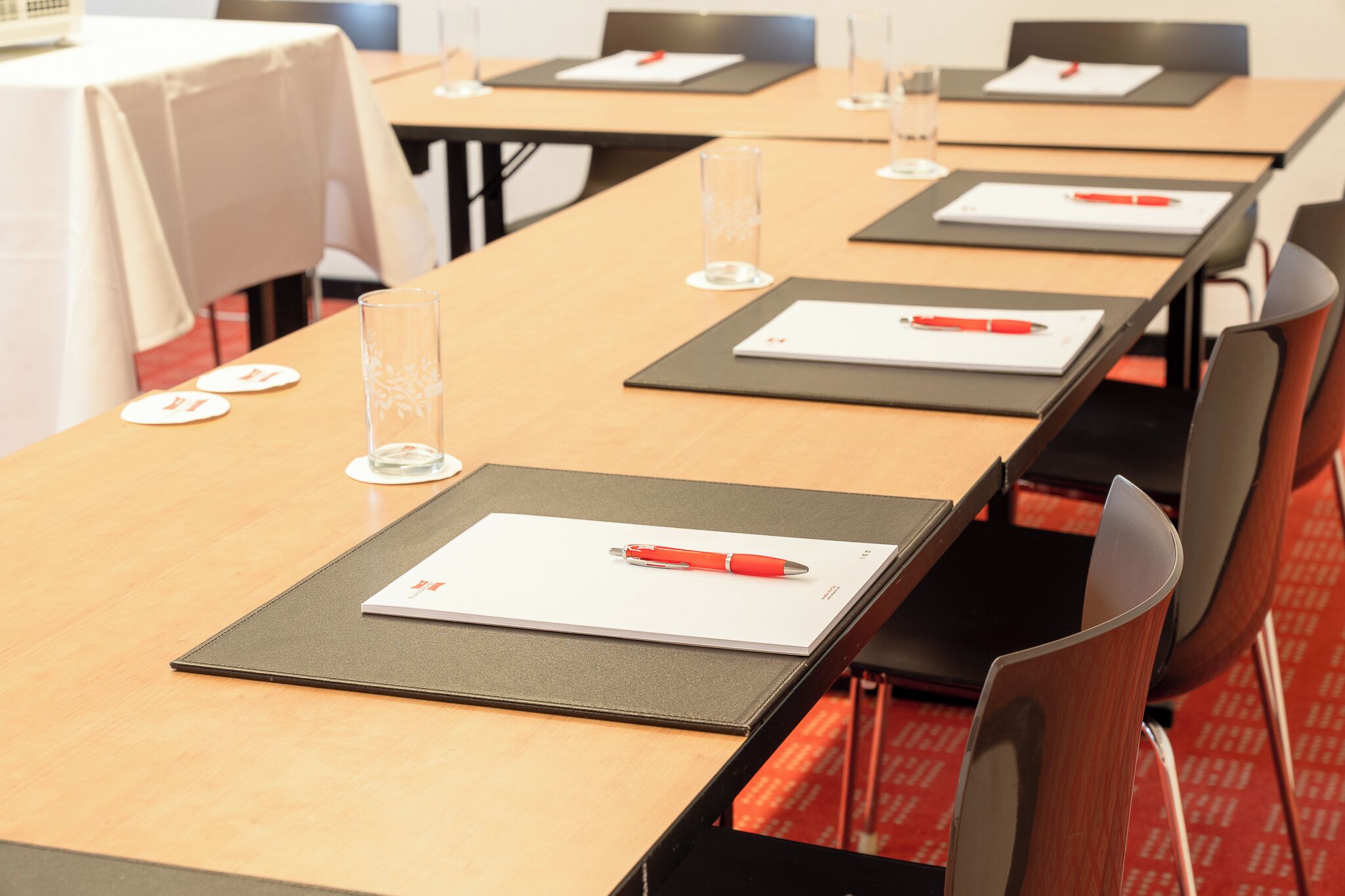 A conference room with long tables, each with a notepad, pen, and glass of water.