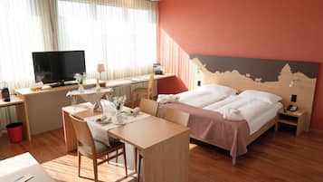 A hotel room with a bed, desk, chair, TV, and a painting on the wall.