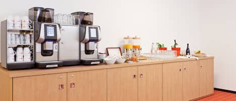 A buffet setup with coffee machines, a juice dispenser, and various food and drink containers.