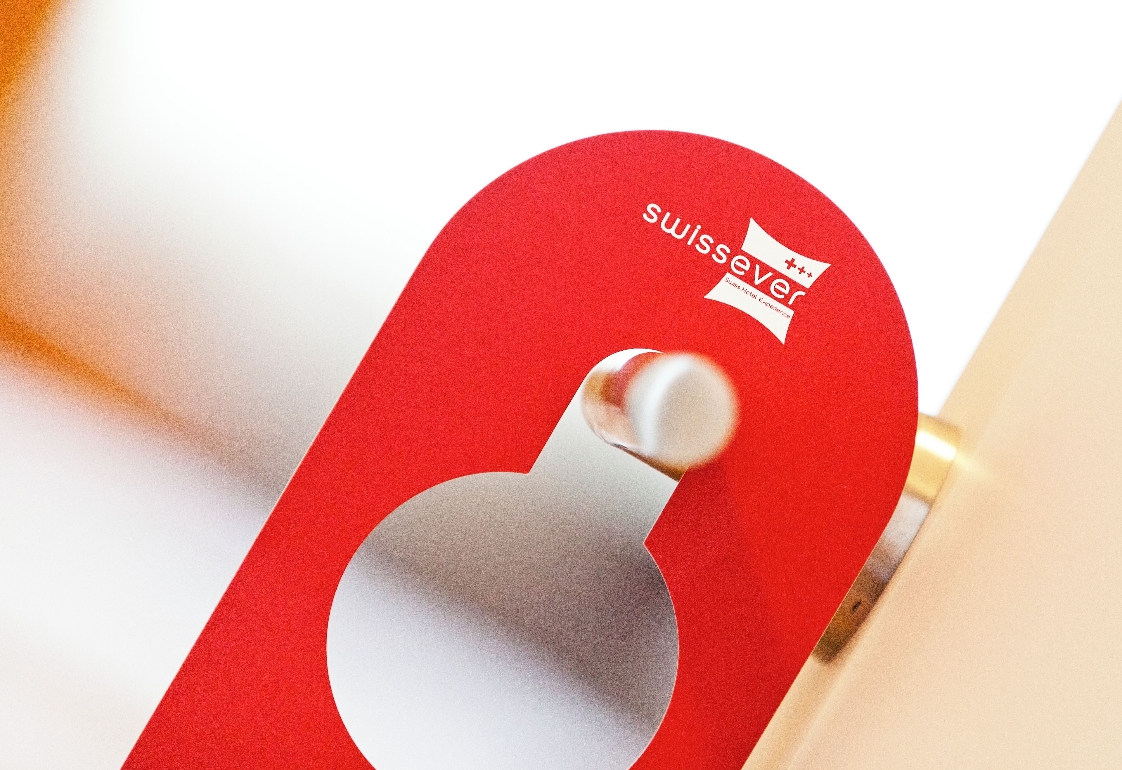 A red metal object with a hole, possibly a part of a door or furniture, with a logo and text that reads "swissever".