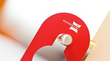 Un objet métallique rouge, doté d’un trou, qui pourrait être une pièce d’une porte ou d’un meuble, et qui porte un logo ainsi que le texte « swissever ».