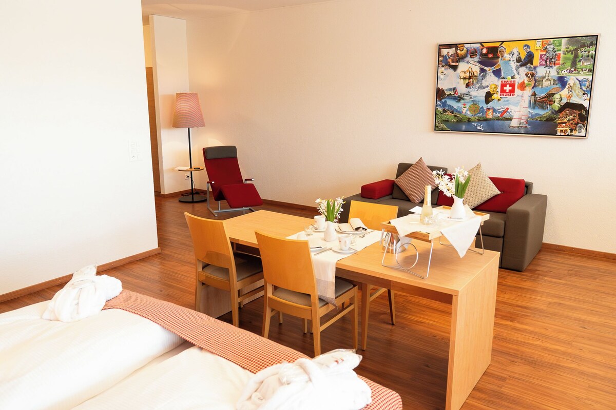 A hotel room with a dining table set for two, a sofa, and a painting on the wall.