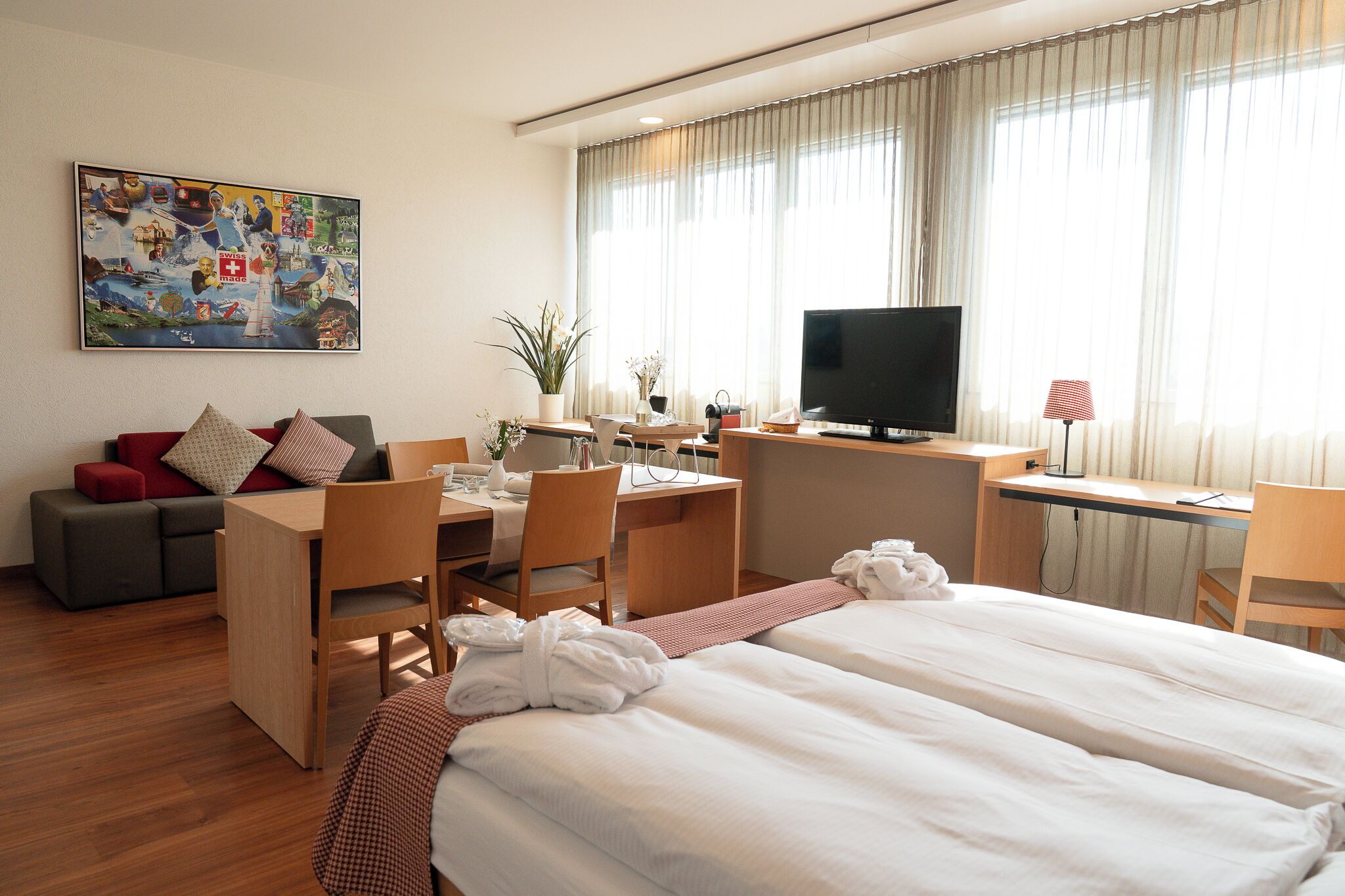 A hotel room with two beds, a desk, a TV, and a painting on the wall.
