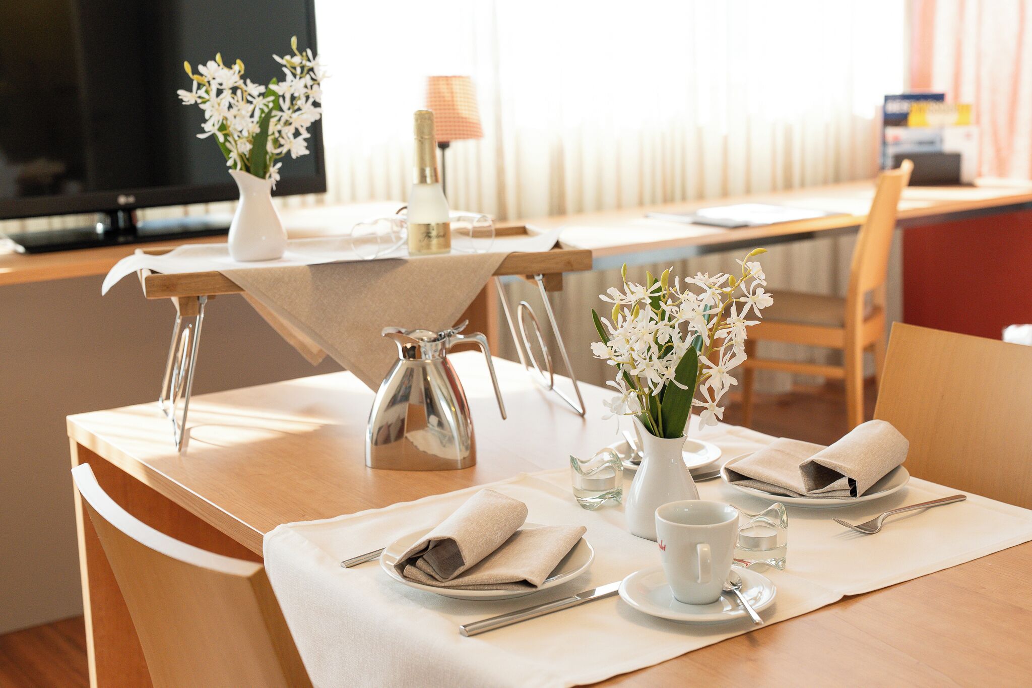A neatly set dining table with a pitcher, a vase with flowers, a cup, and a plate with a napkin.