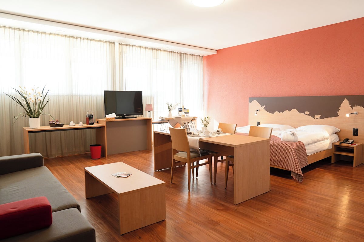 A modern hotel room with a bed, desk, and seating area.
