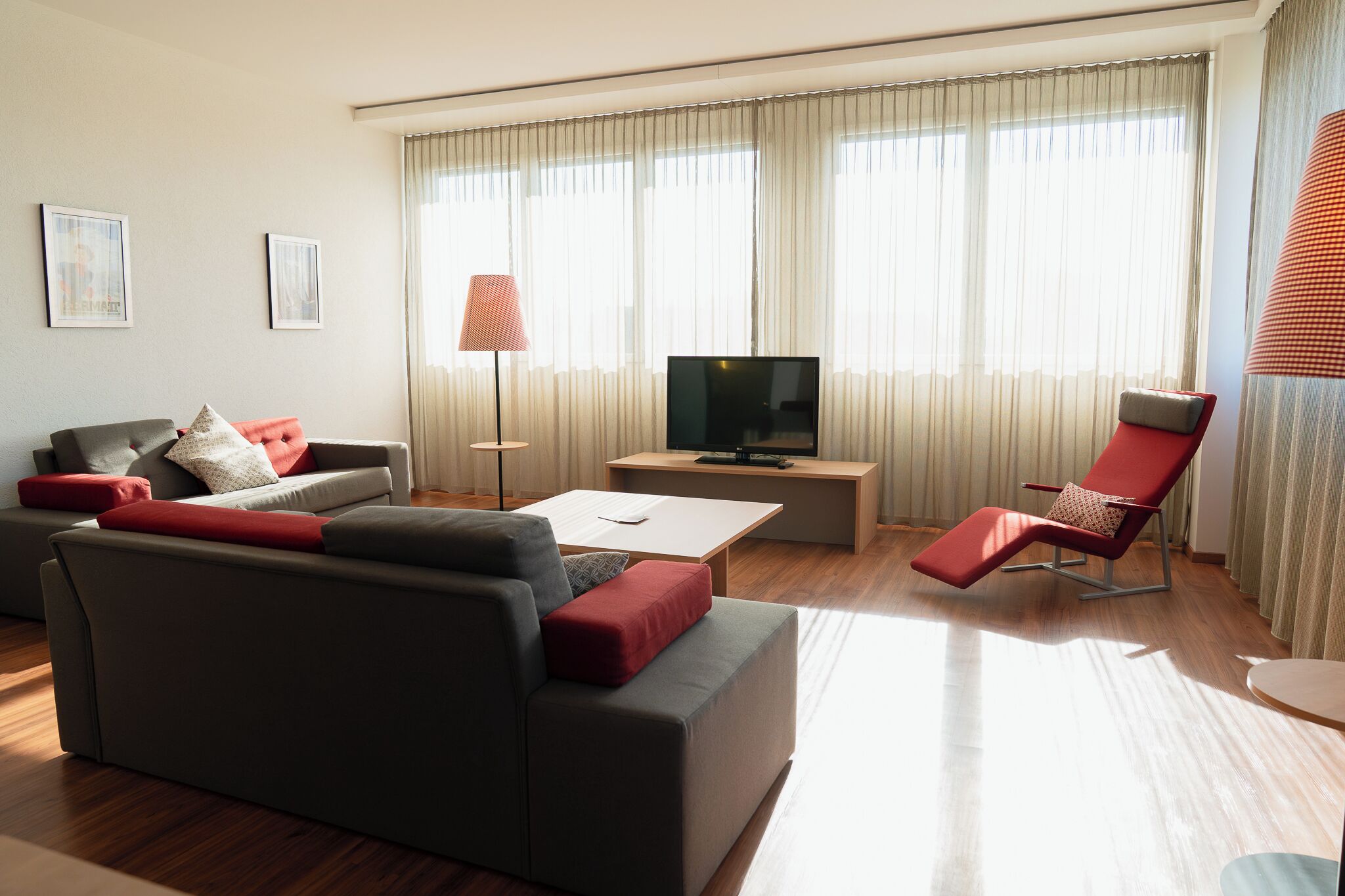 Una sala de estar moderna con un sofá, un televisor, una mesa de centro y una silla roja.