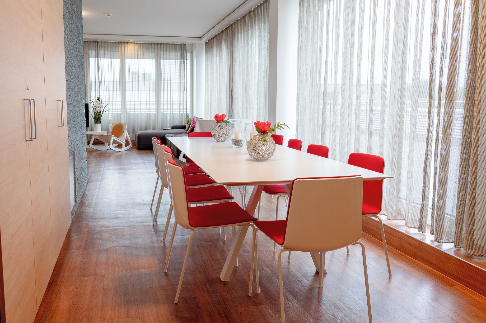 A modern dining area with a long table, red chairs, and decorative vases.