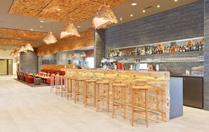 A bar area with wooden bar stools, a counter with a wine cooler, and a wall of liquor bottles. - SwissEver Hotel Zug (Cham)