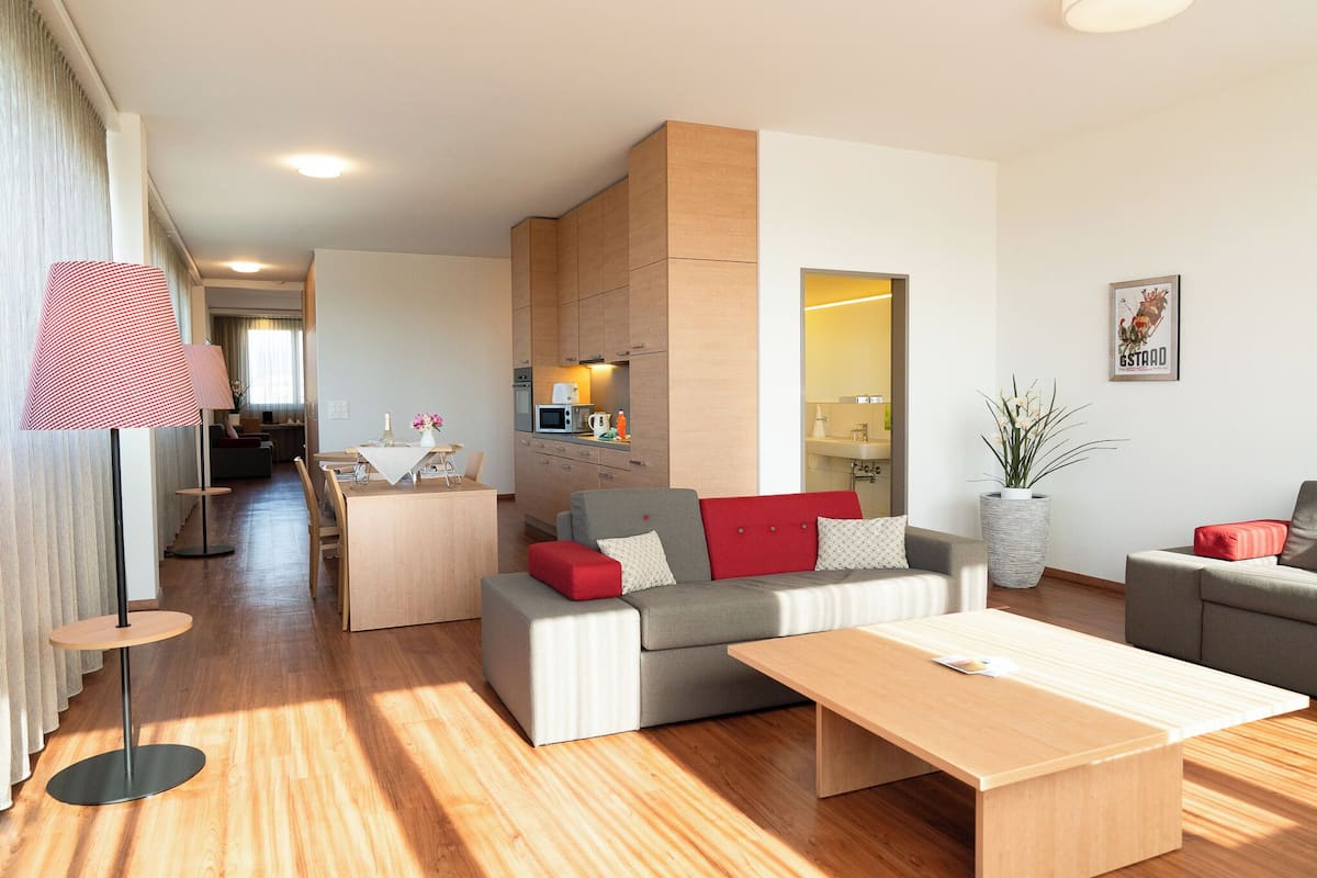 A modern living room with a grey sofa, red cushions, a wooden coffee table, and a dining area with a table and chairs.