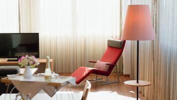 Une chambre d’hôtel moderne avec un fauteuil rouge, une petite table ronde, un téléviseur et une lampe sur pied.