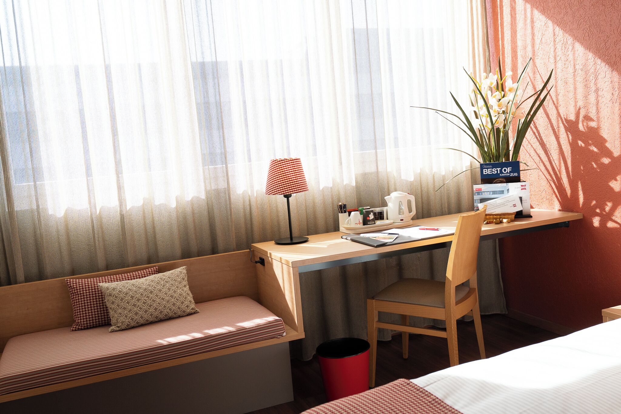 A hotel room with a desk, chair, and a small seating area with cushions.