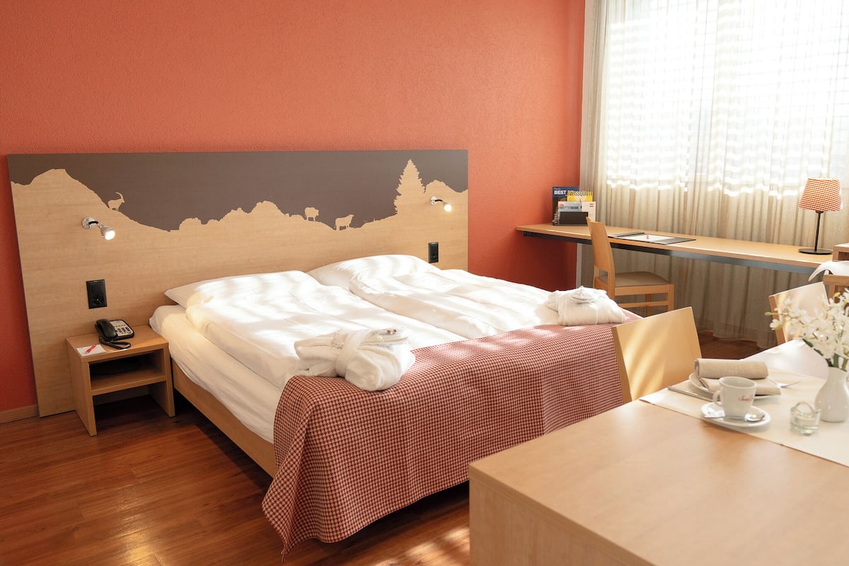 A hotel room with a bed, a desk, a chair, a table, and a window with curtains.
