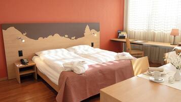 Ein Hotelzimmer mit Bett, Schreibtisch, Stuhl, Tisch und einem Fenster mit Vorhängen.