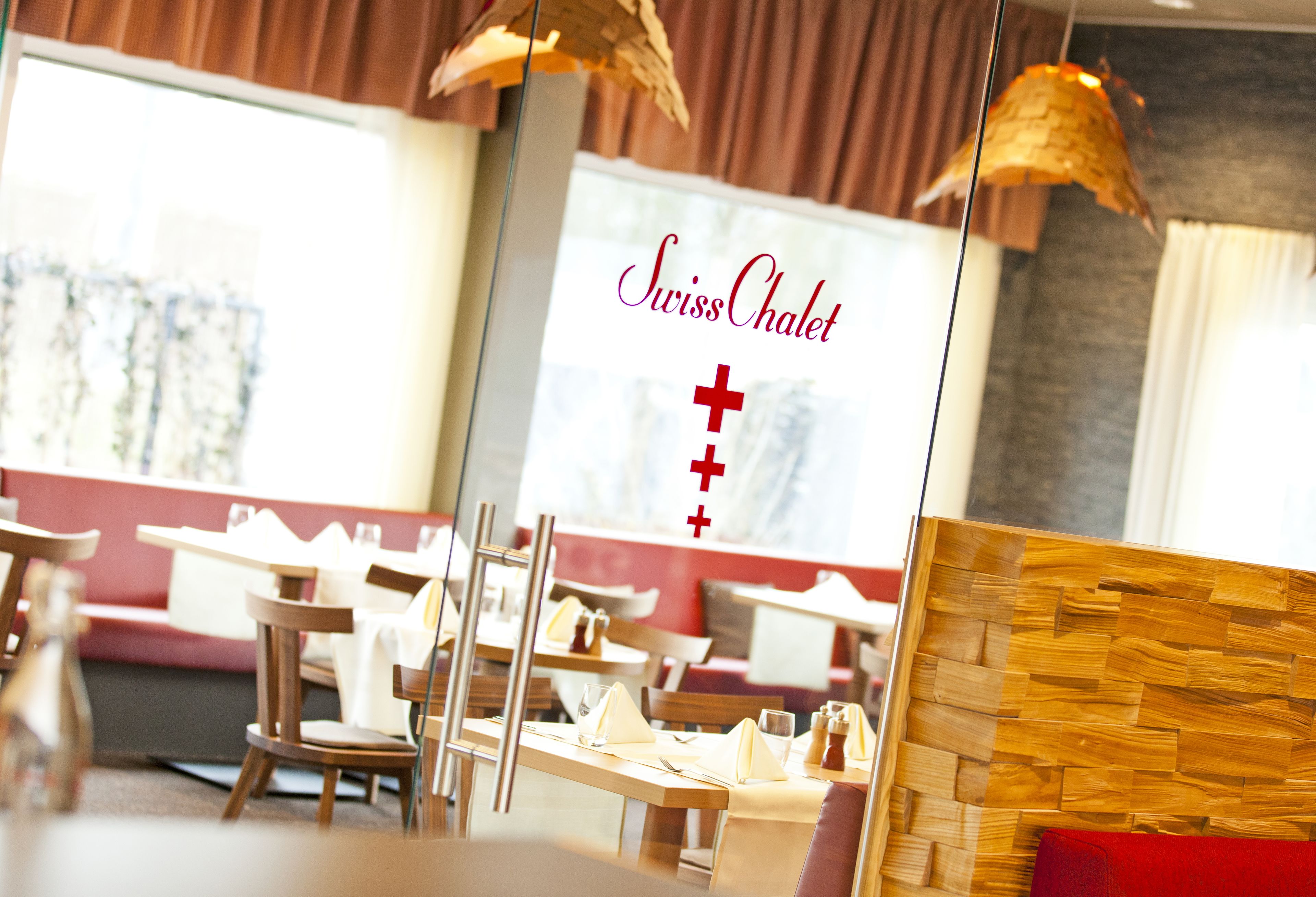 A restaurant interior with wooden tables and chairs, a red cushioned bench, and hanging pendant lights.