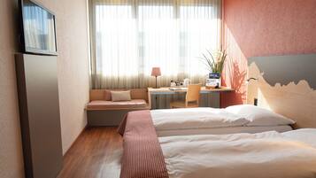 A hotel room with a bed, a desk, a chair, a TV, and a window with curtains.