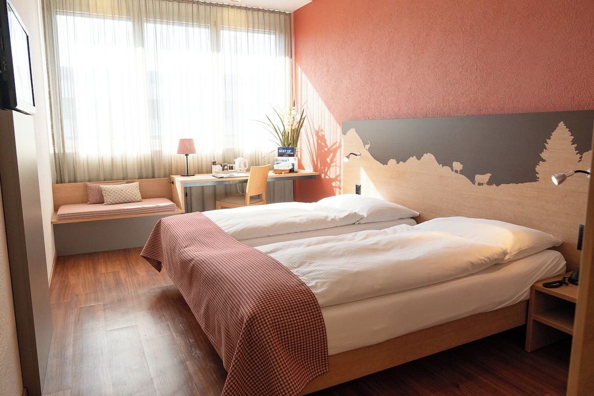 A hotel room with a bed, a desk, a chair, and a window with curtains.