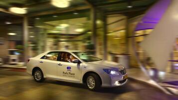 A white car with 'Park Plaza' branding parked in front of a building with large glass windows and a purple accent wall.