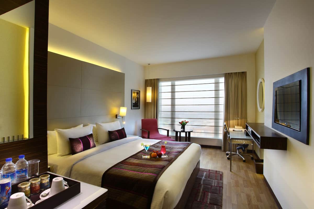 A hotel room with a large bed, a desk, a chair, a TV, and a window with curtains.