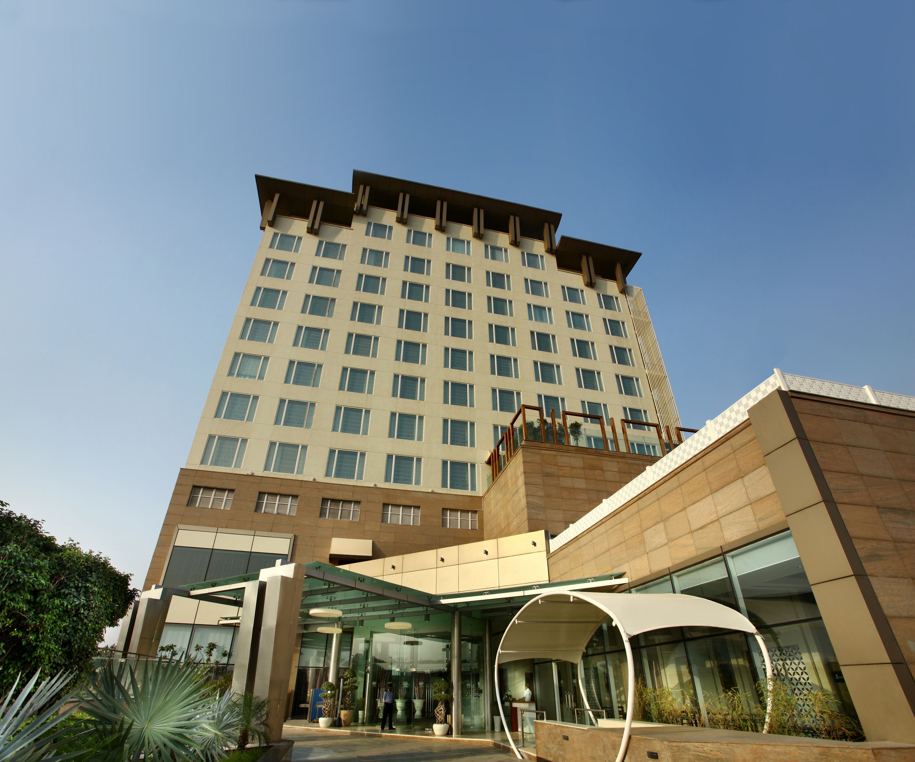 Ein modernes Hotel mit Glaseingang, überdachtem Außenbereich und einem hohen Gebäude im Hintergrund.