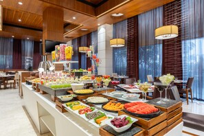 Un buffet proposant une variété de plats et de boissons, un téléviseur et un espace détente avec des tables et des chaises.