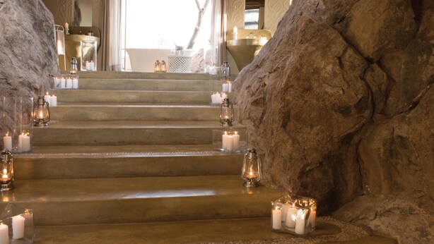 Una escalera con velas y faroles que lleva a un área de baño con lavabo y espejo.