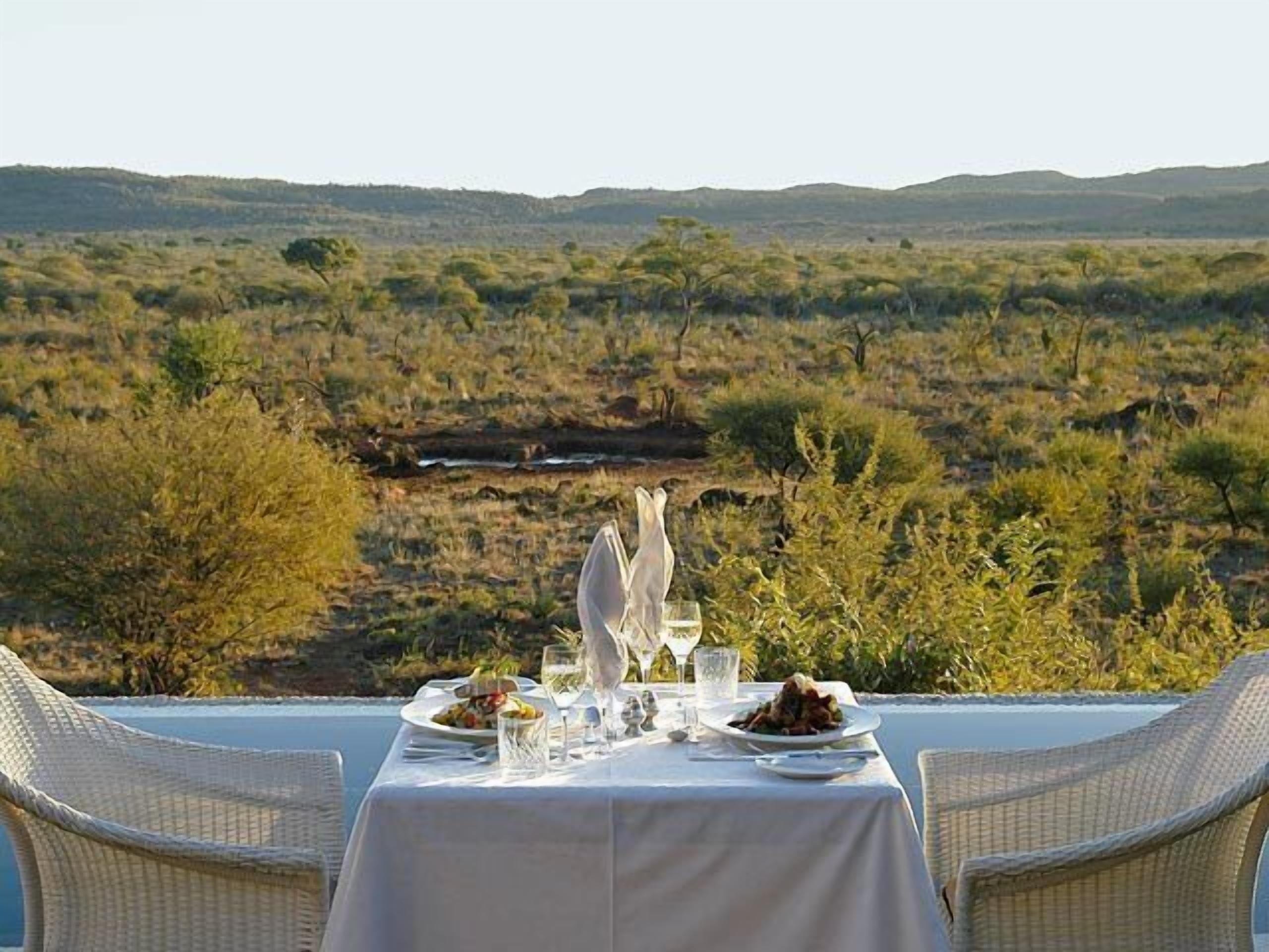 A table set for two with a view of a savanna landscape.