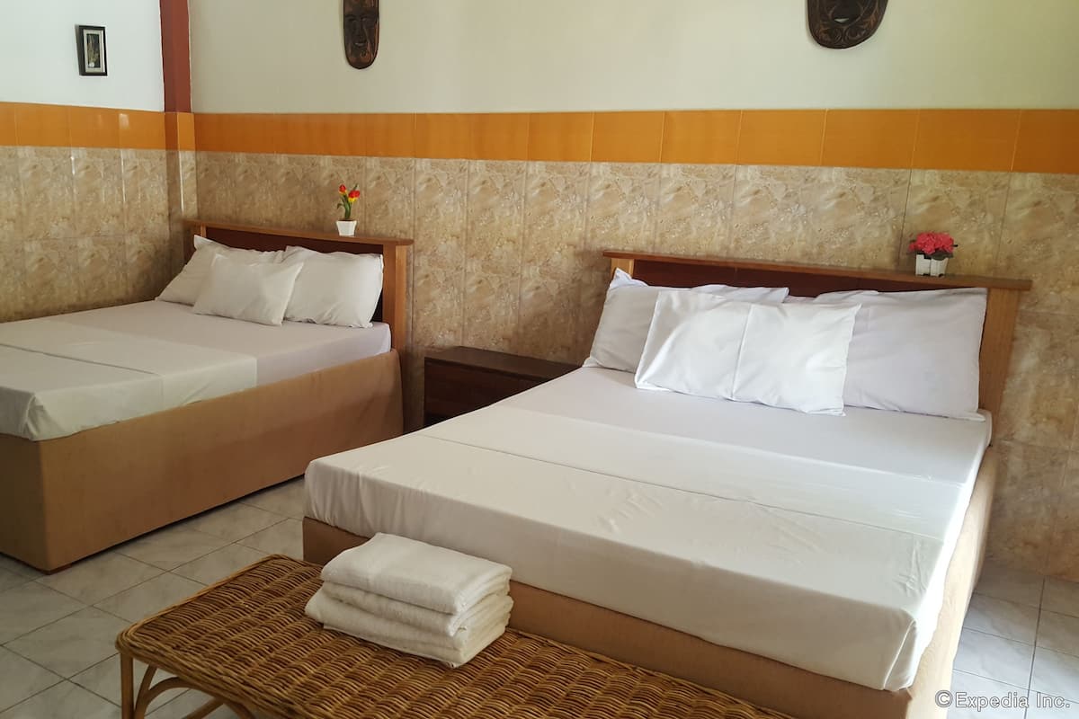 Two single beds with white linens, a small table with folded towels, and a decorative vase with flowers on the headboard.