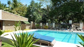 A swimming pool with a stone wall, a lounge chair, and tropical plants. - Cooper's Beach Resort (Puerto Princesa)