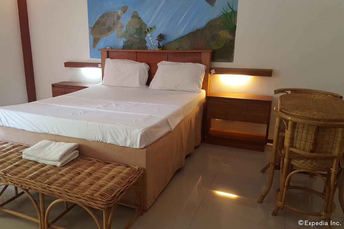 A hotel room with a large bed, two bedside tables, a wicker bench, a chair, and a mural of sea creatures on the wall.