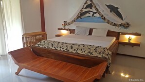 A bedroom with a wooden bench, a bed with a floral bedspread, a wall mural of dolphins, and bedside lamps. - Cooper's Beach Resort (Puerto Princesa)
