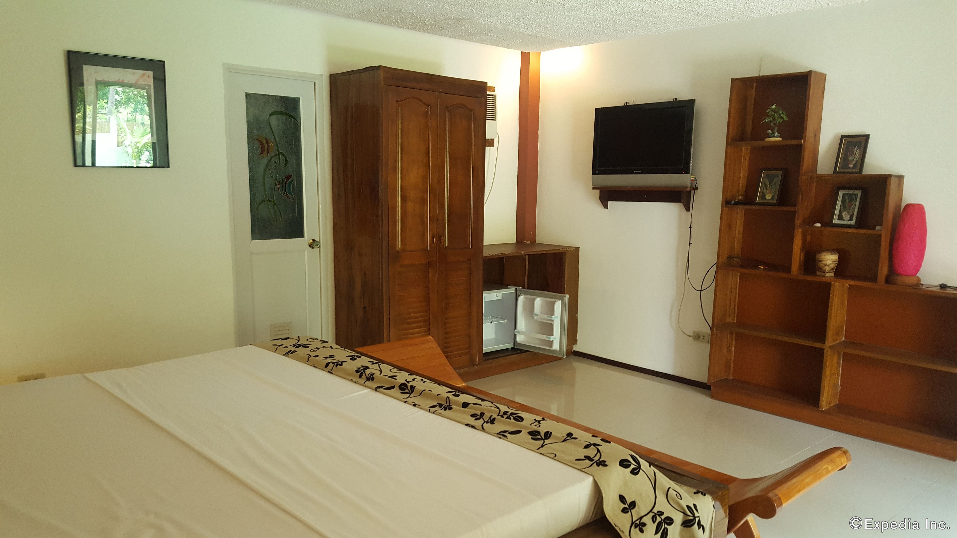 Un dormitorio con cama, armario, televisor y estanterías con objetos.