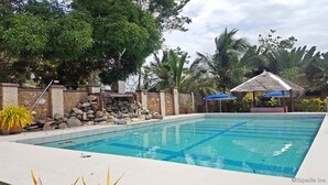 A swimming pool with a stone wall, a thatched-roof structure, and a blue umbrella. - Cooper's Beach Resort (Puerto Princesa)