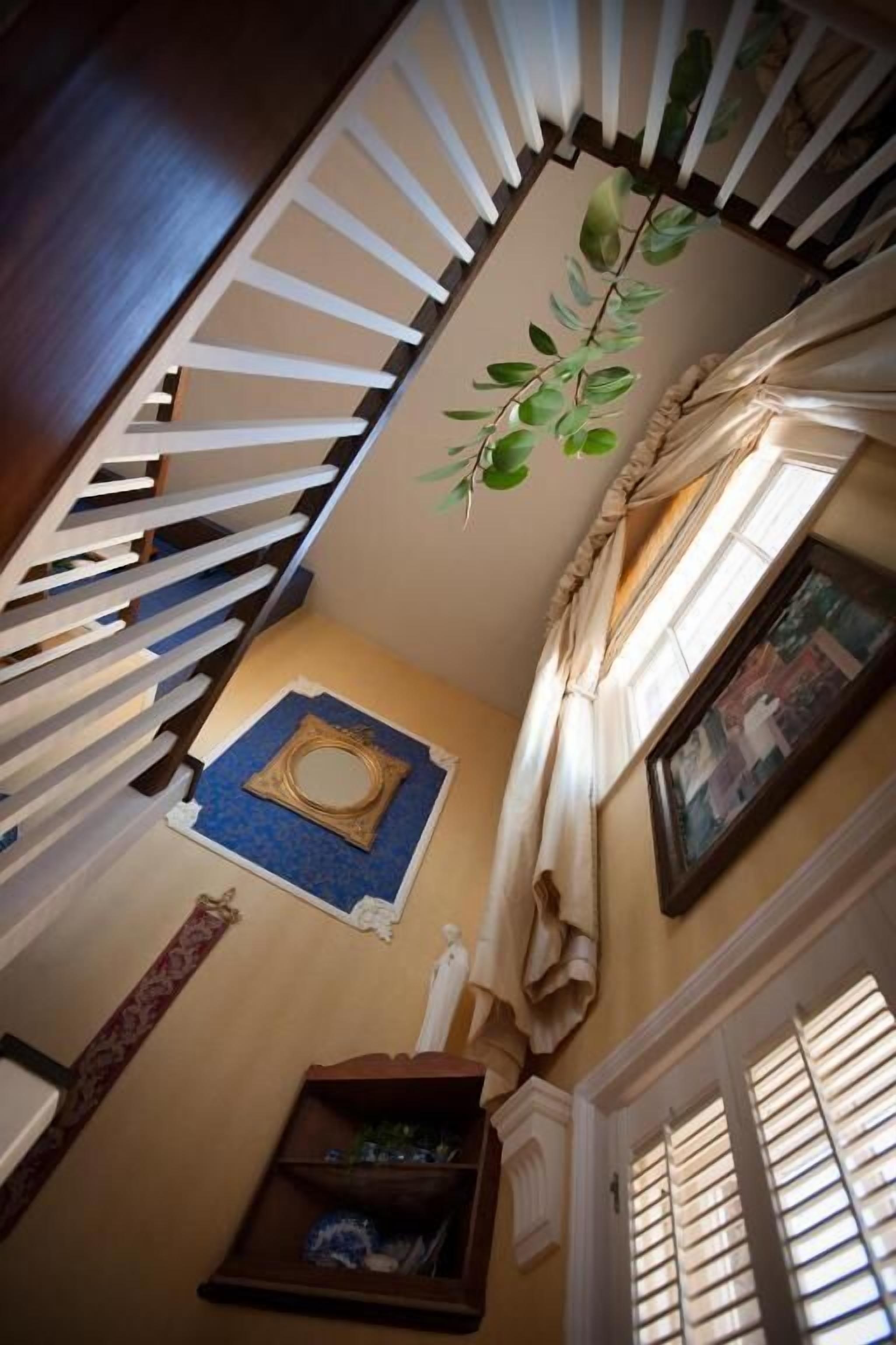A staircase with a white railing, a blue mat, a framed mirror, and a window with curtains.