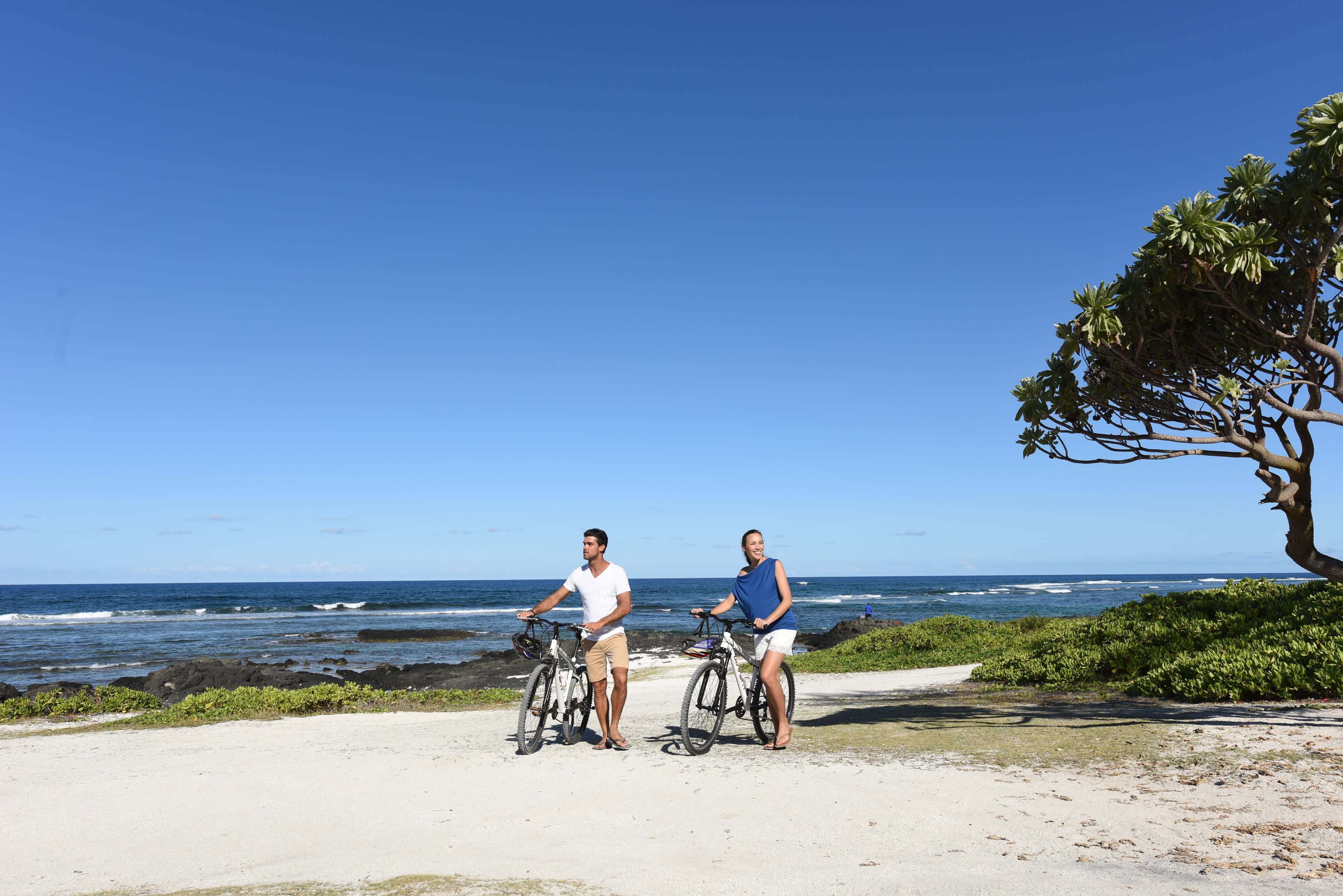 Dos personas en bicicletas cerca de una playa con cielo despejado.