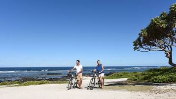 Dos personas en bicicletas cerca de una playa con cielo despejado.